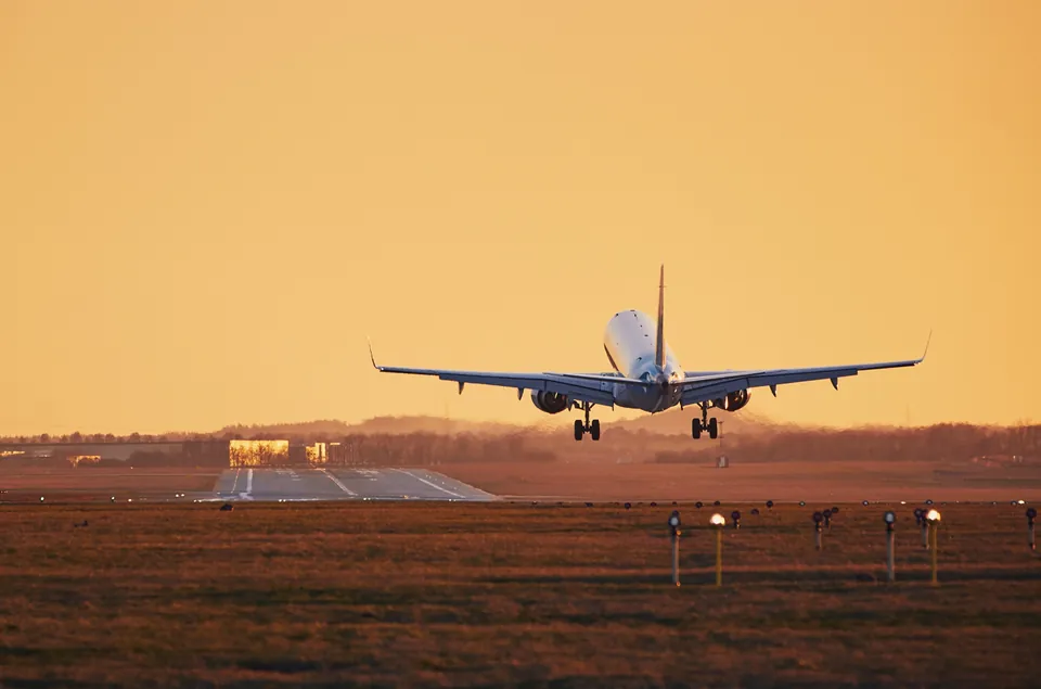A passenger jet coming in to land at sunset, with the runway and approach lights ahead.