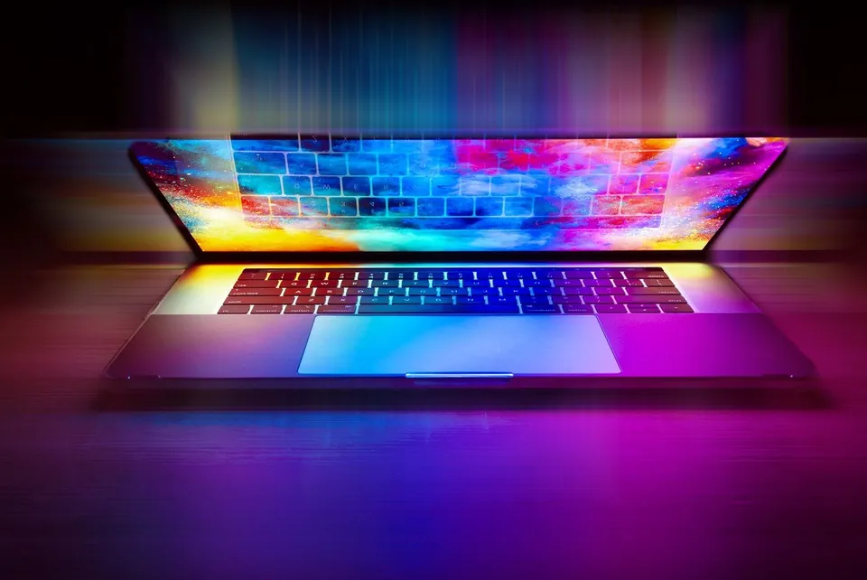 An open laptop glowing with vivid colour in a dark room.